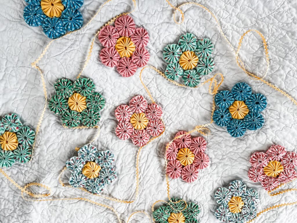 Flower garland made from quilted yo-yos and the Playtime 30's fabric strung on Lori Holt's Vintage Trim over a background of a light gray quilt.